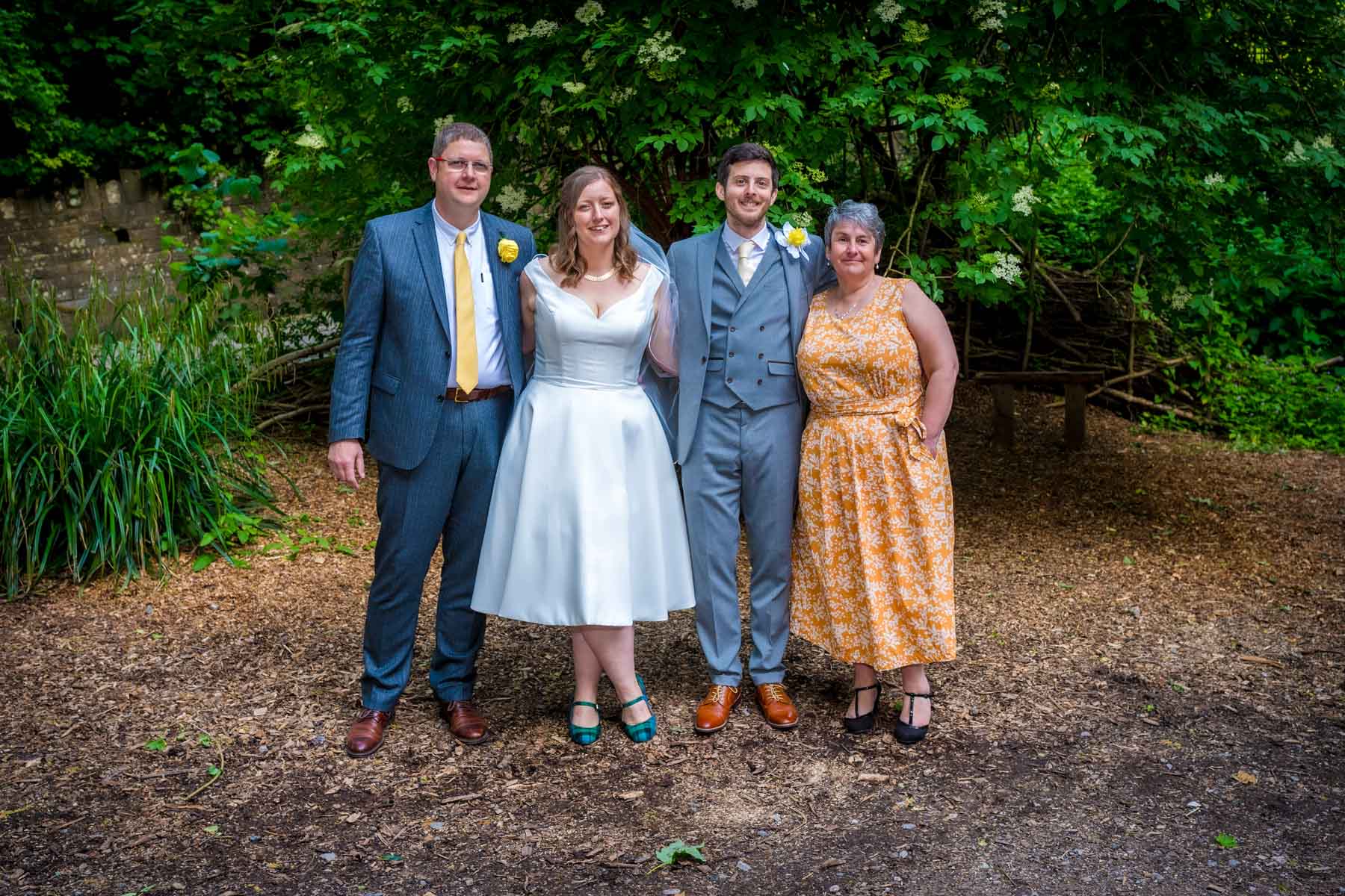 Newlyweds posing with brides parents in woodlands.