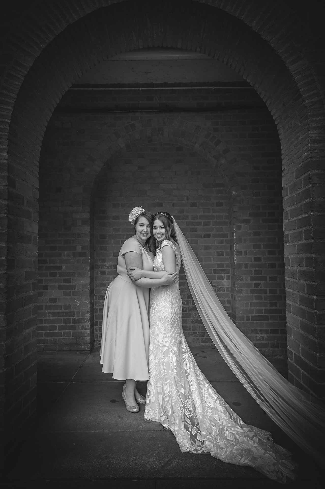 Bride and sister holding each other under arch
