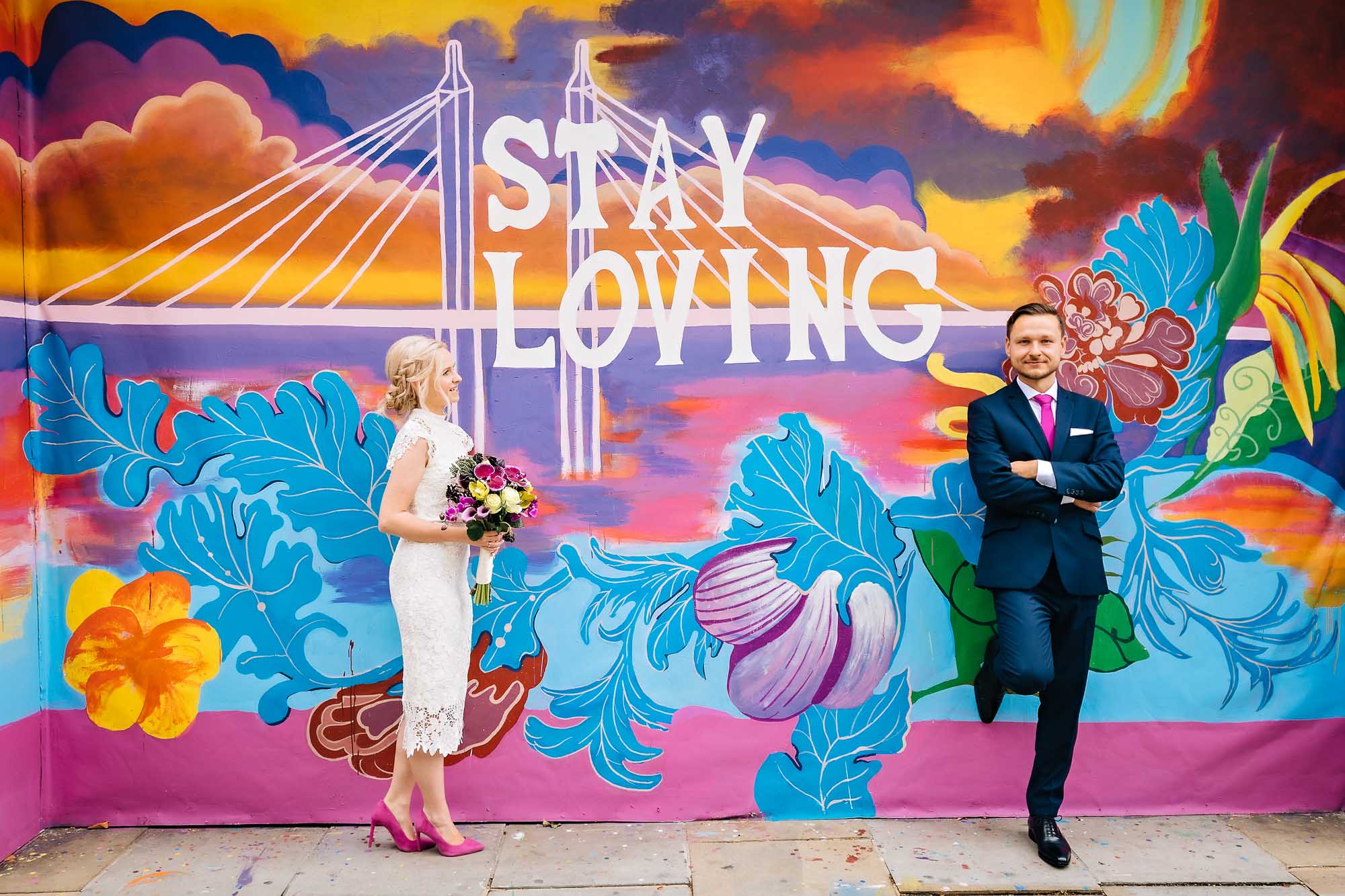 Bride and groom in front of vibrant 'Stay Loving' mural in Chelsea, London